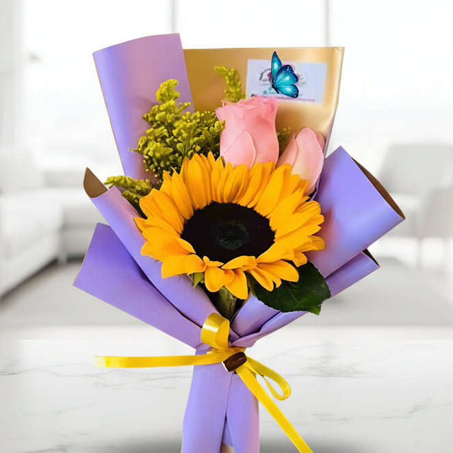 Mini bouquet with 1 sunflower and 2 pink roses in lilac and gold paper with yellow ribbon – Arboletes delivery