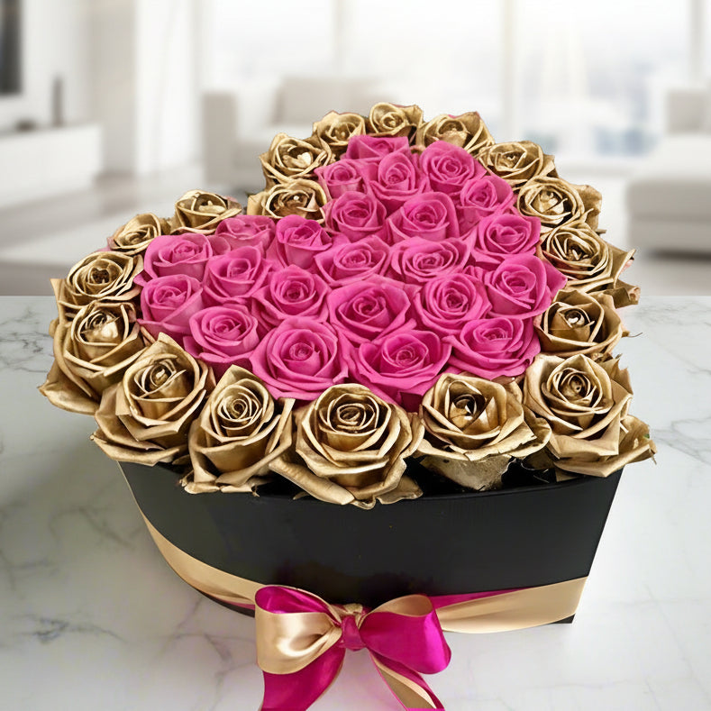 Heart-shaped arrangement of pink and gold roses in a box on a marble surface