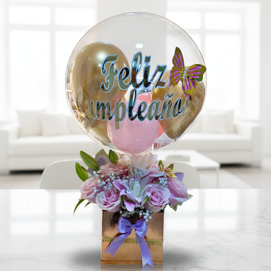 Birthday gift with clear balloon that says “Feliz Cumpleaños” and pink flowers in a gold box with purple ribbon – Arboletes delivery