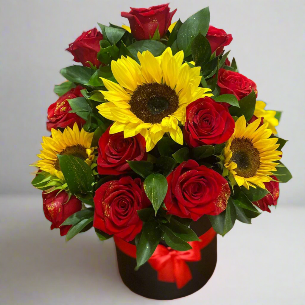 Floral arrangement with bright sunflowers and red roses in a black hat box with red ribbon – Same-day delivery in Acacías, Meta