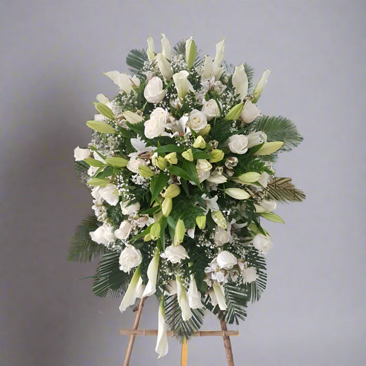 Standing funeral spray with white roses, lilies, calla lilies, and greenery – available for delivery in all cities of Colombia.