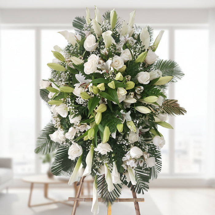 Standing funeral spray with white roses, lilies, calla lilies, and greenery – available for delivery in all cities of Colombia.