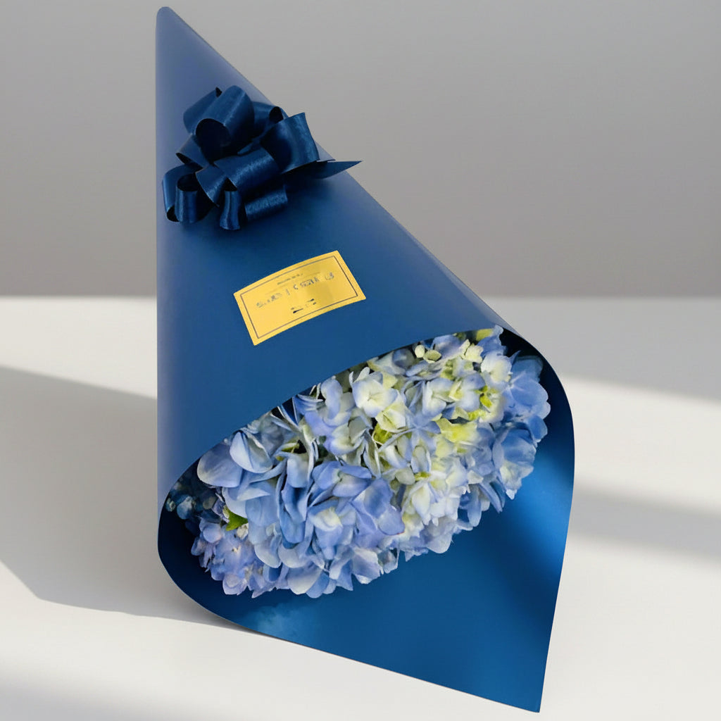 Blue hydrangea bouquet wrapped in navy paper with bow – elegant gift for him, available for delivery in Medellín.