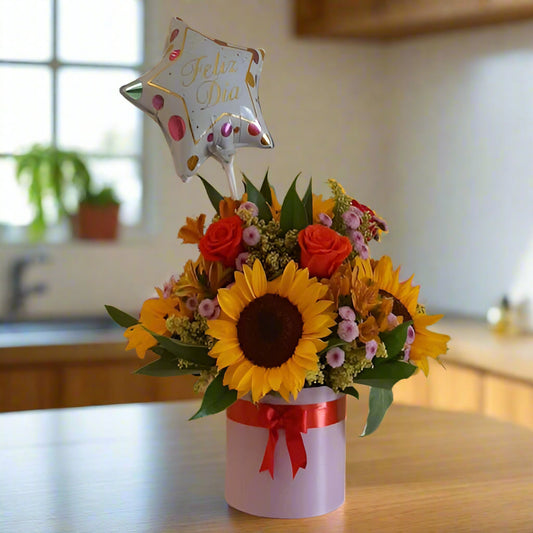 Bright birthday floral arrangement with sunflowers, multicolor roses, seasonal flowers, and a transparent 'Feliz Cumpleaños' balloon in a black box. Perfect for delivery in Cali.