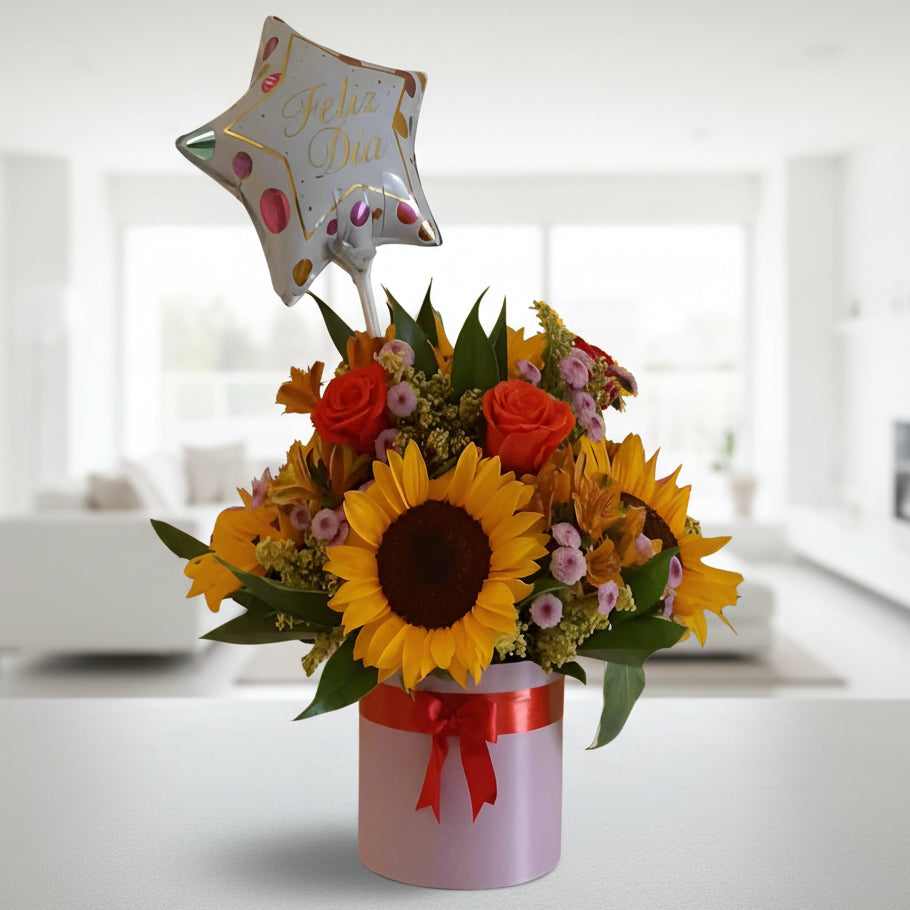 Bright birthday floral arrangement with sunflowers, multicolor roses, seasonal flowers, and a transparent 'Feliz Cumpleaños' balloon in a black box. Perfect for delivery in Cali.