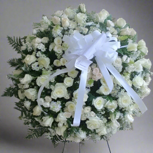 Elegant standing funeral wreath made of white roses, greenery, and a large white ribbon – available for delivery across Colombia.