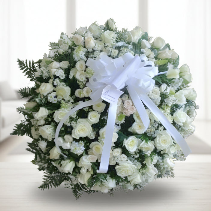 Elegant standing funeral wreath made of white roses, greenery, and a large white ribbon – available for delivery across Colombia.