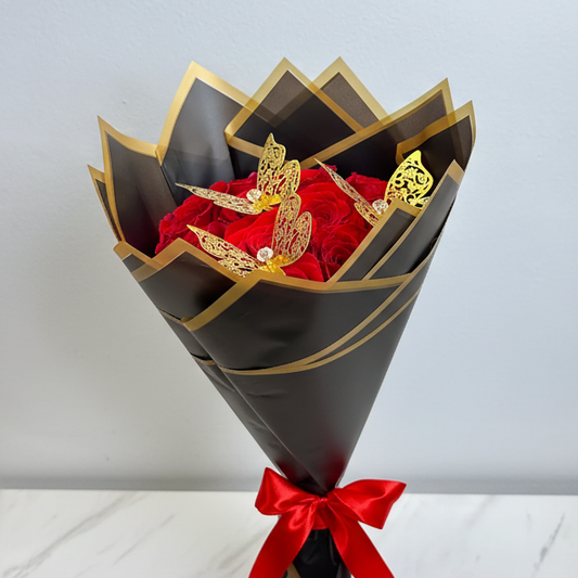 Elegant bouquet of 12 red roses decorated with golden butterfly accents, wrapped in premium Korean-style black paper with gold trim, available for delivery in Medellín, Colombia.