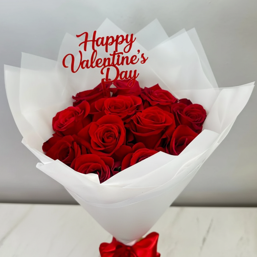 Romantic bouquet of 12 red roses wrapped in white paper, finished with a red satin bow and a red “Happy Valentine’s Day” sign, perfect for Valentine’s gifting.