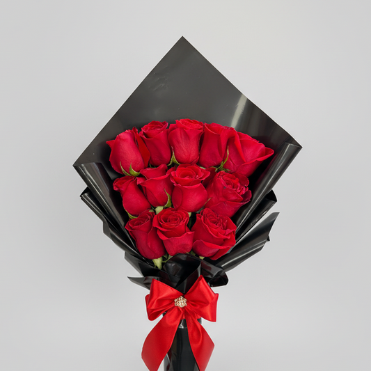 Elegant bouquet of 12 red roses wrapped in premium black Korean-style paper, finished with a red satin bow, perfect for romantic gifting.