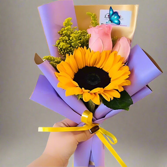 Mini bouquet with 1 sunflower and 2 pink roses in lilac and gold paper with yellow ribbon – Arboletes delivery