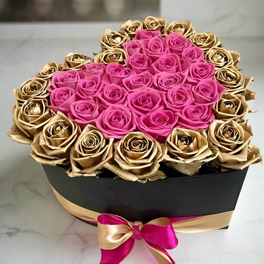 Heart-shaped arrangement of pink and gold roses in a box on a marble surface