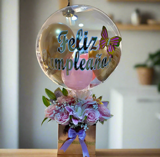 Birthday gift with clear balloon that says “Feliz Cumpleaños” and pink flowers in a gold box with purple ribbon – Arboletes delivery