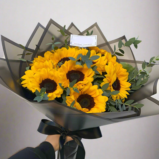 Bouquet of 8 yellow sunflowers with eucalyptus in black Korean paper wrap and black ribbon – Arboletes delivery