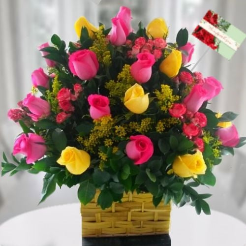 Floral arrangement with yellow and fuchsia roses in a yellow basket, with mini carnations and greenery