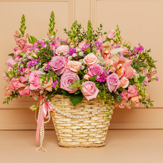 Elegant Mother’s Day basket arrangement with pink roses, orchids, snapdragons, and seasonal flowers in a pearl-accented woven basket.