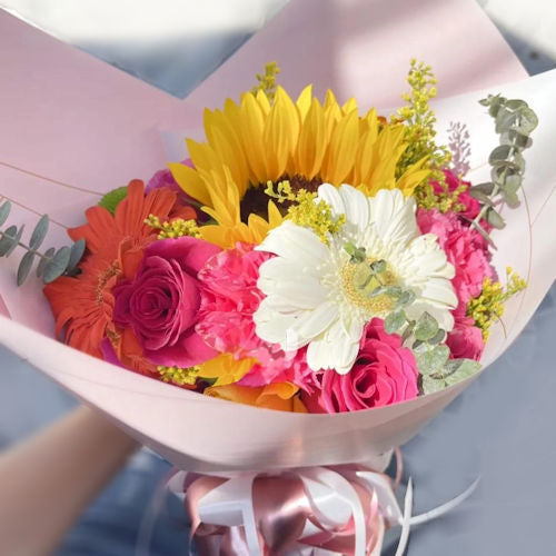 Vibrant bouquet of colorful gerberas, sunflowers, pink roses, and greenery, elegantly wrapped with a ribbon. Perfect for delivery in Cartago, Valle.
