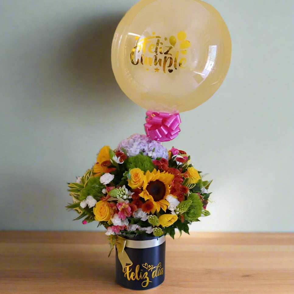 Charming birthday floral arrangement with multicolor roses, seasonal flowers, and a transparent 'Feliz Cumpleaños' balloon in a pink hatbox. Perfect for delivery in Cali.