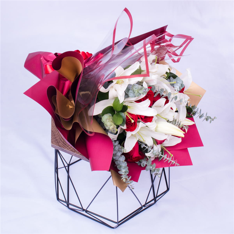 Elegant bouquet of white lilies and red roses wrapped in Korean paper with ribbon, perfect for delivery in Medellín.