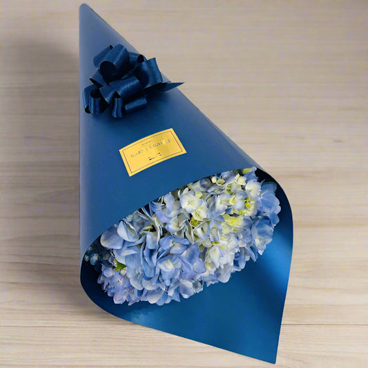 Blue hydrangea bouquet wrapped in navy paper with bow – elegant gift for him, available for delivery in Medellín.

