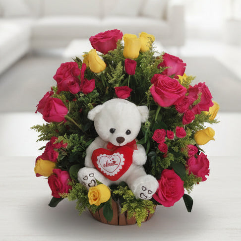 Colorful floral arrangement with pink and yellow roses surrounding a white teddy bear holding a heart, ideal for flower delivery in Bucaramanga, Colombia.