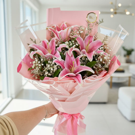 Bouquet of pink flowers with a pink wrap held by a person indoors.