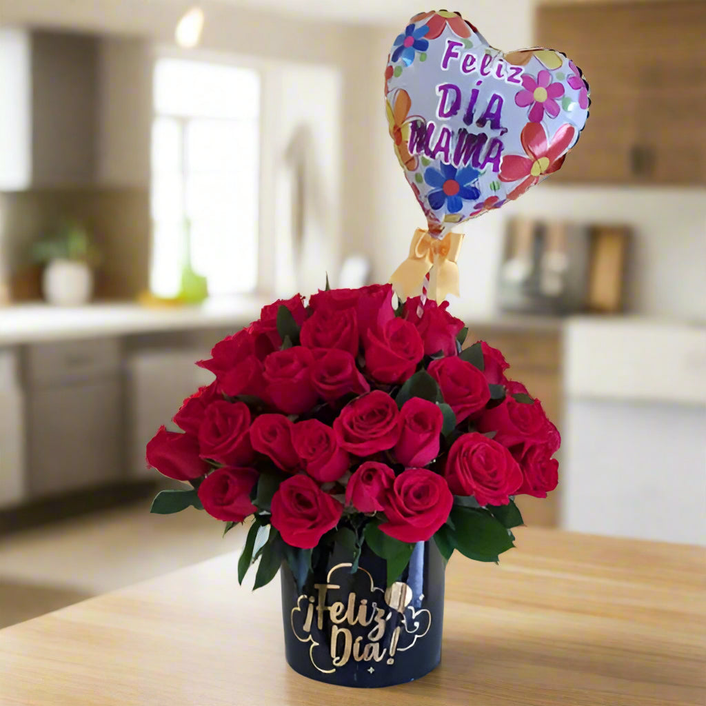 Elegant arrangement of fresh red roses in a black box with 'Feliz Día' in gold lettering, accompanied by a heart-shaped balloon that says 'Feliz Día Mamá.' Perfect gift for Mother's Day with same-day delivery in Cali.