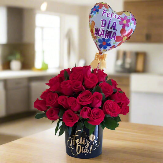 Elegant arrangement of fresh red roses in a black box with 'Feliz Día' in gold lettering, accompanied by a heart-shaped balloon that says 'Feliz Día Mamá.' Perfect gift for Mother's Day with same-day delivery in Cali.