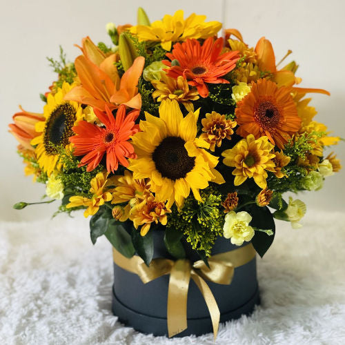 Beautiful round box with sunflowers, lilies, daisies, gerberas, carnations, and pompoms with a decorative bow
