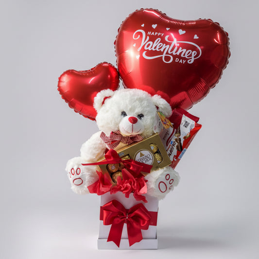 Valentine’s Day gift featuring a white teddy bear with Ferrero Rocher chocolates, heart-shaped balloons that say “Happy Valentine’s Day,” and decorative red bows, available for delivery in Medellín, Colombia.