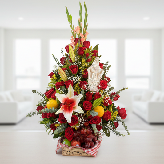 Triangular floral arrangement with Virgin Mary figure, red roses, lilies, seasonal greenery and fresh fruit basket in Bucaramanga